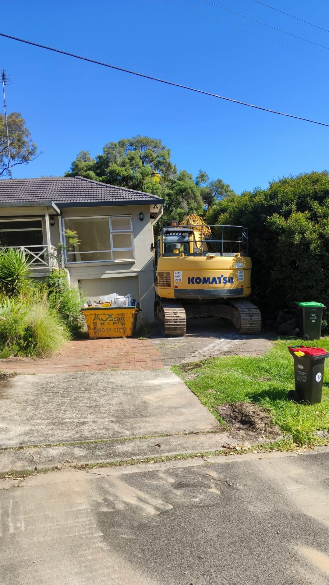 Komatsu excavator on residential driveway with skip bin